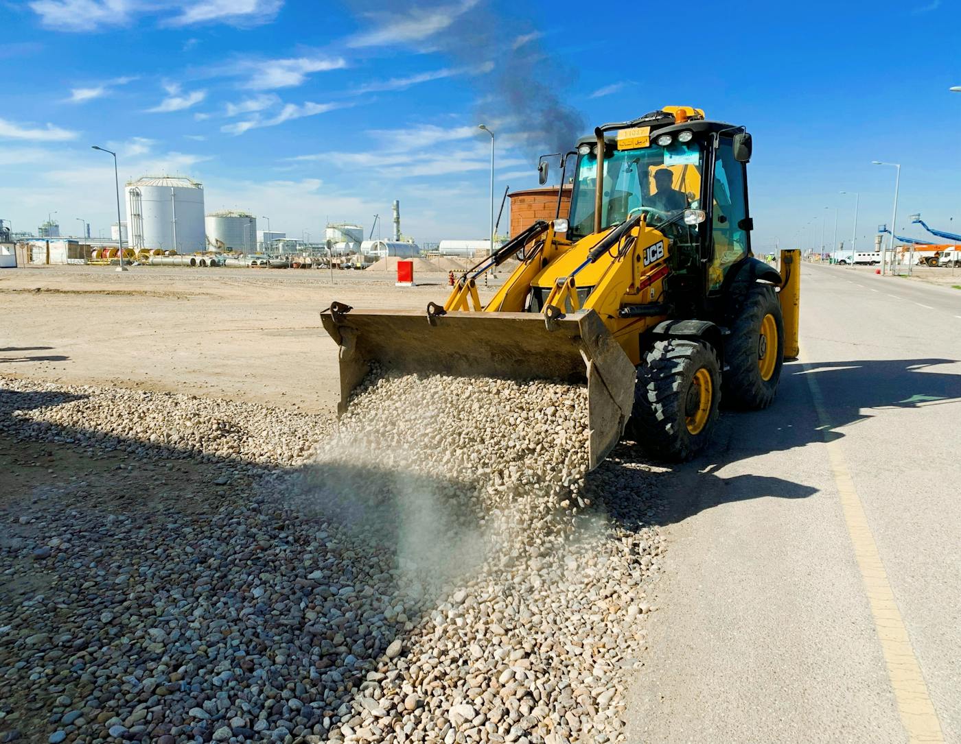 Fagartikler 4 A yellow excavator unloading pebbles on a road at an industrial construction site under a clear blue sky.