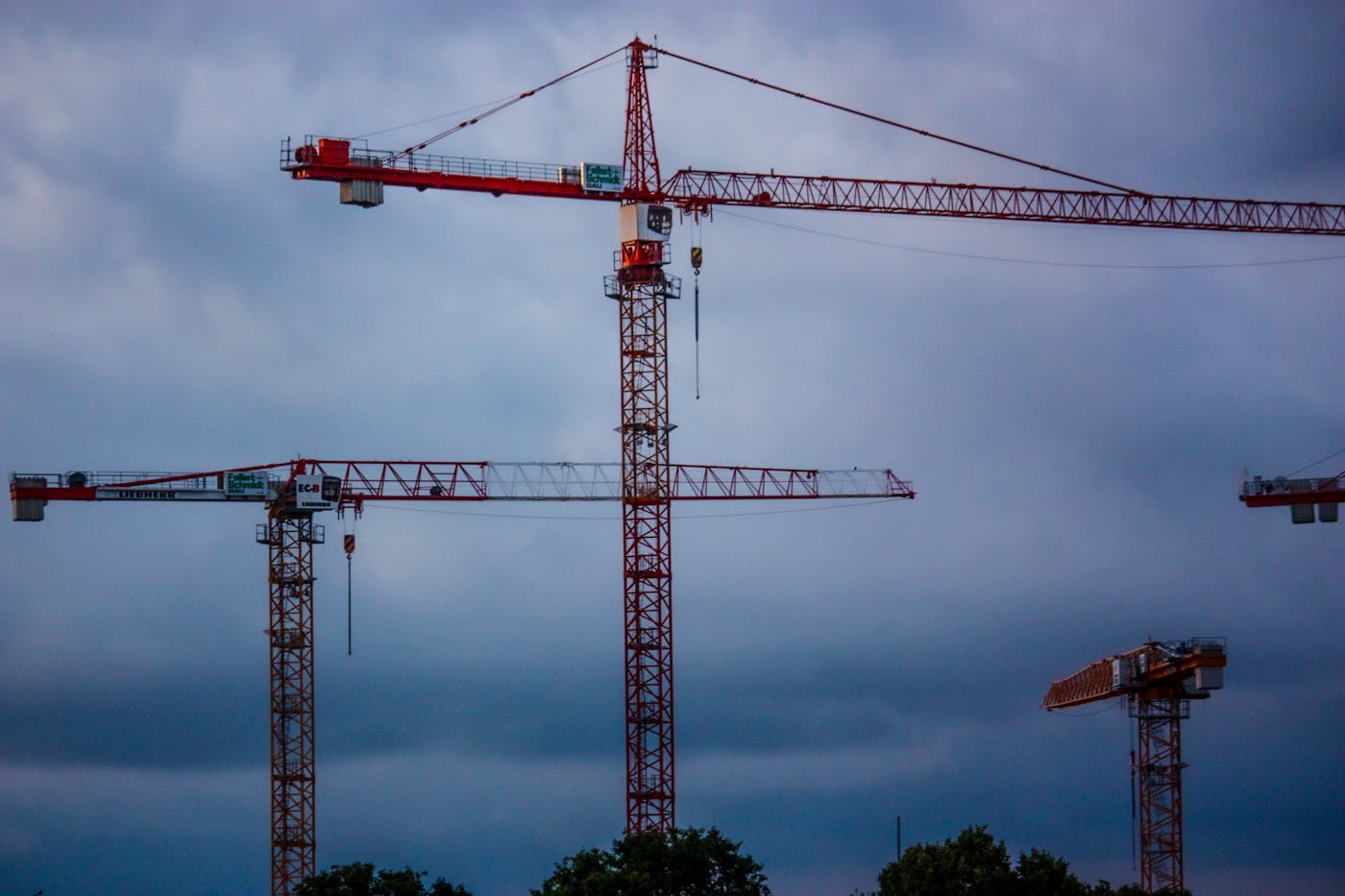 Fagartikler 3 Tower cranes stand tall under a dramatic cloudy sky, representing modern industry.